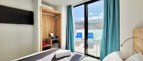 Habitación de hotel con cama, escritorio, armario y balcón con vistas a la ciudad.
