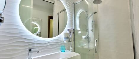 A modern bathroom with a round mirror, a glass-enclosed shower, and a white sink.