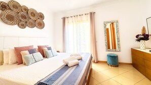 A bedroom with a bed, curtains, a mirror, a vase, and a hanging light fixture.