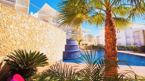 A pool area with a stone wall, palm trees, and a multi-level water feature.