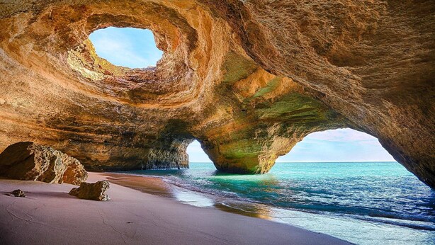 A natural rock formation with a large archway over a beach.