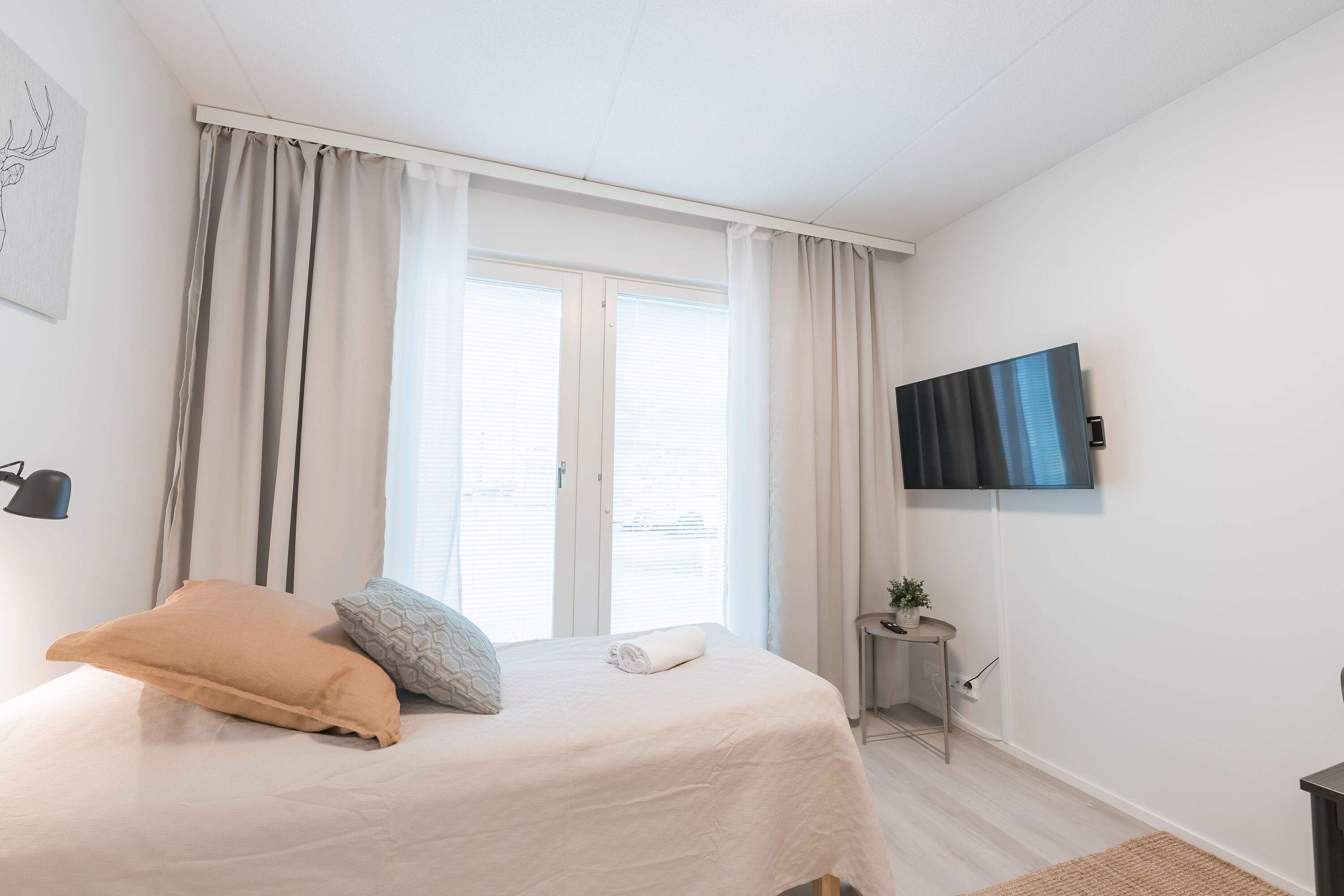 A bedroom with a bed, curtains, a television, and a small table with a plant.