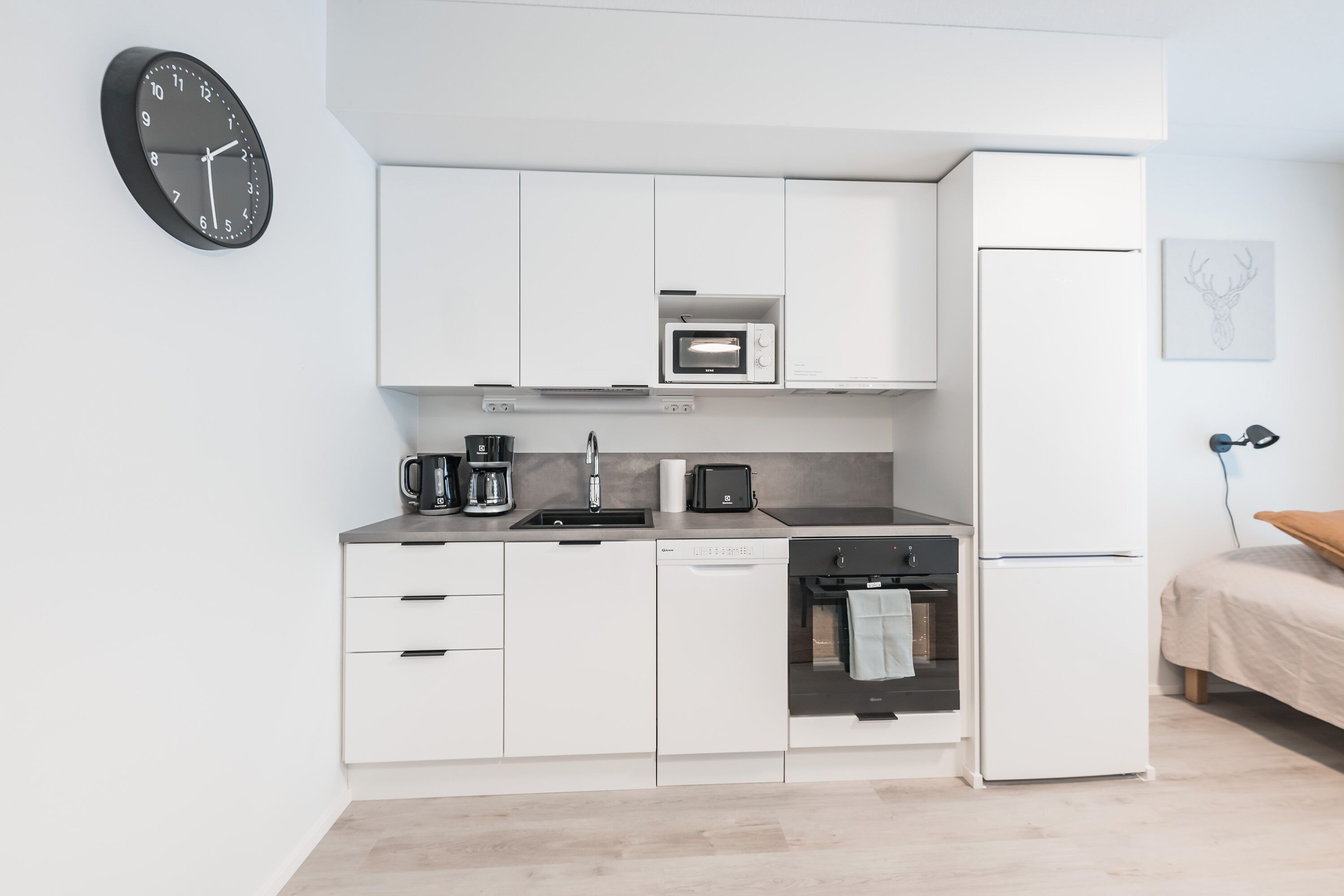 A compact kitchen with white cabinets, a microwave, a coffee maker, a dishwasher, and a refrigerator.