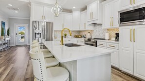 A modern kitchen with white cabinetry, gold handles, a central island with bar stools, and a stainless steel refrigerator.