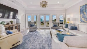 A spacious living room with a large TV, comfortable seating, and a view of the outdoors through glass doors.