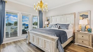 A bedroom with a large bed, a chandelier, a nightstand, and a window with blinds.
