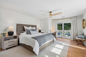 Une chambre à coucher comprenant un lit, des tables de chevet, un bureau, une chaise, un balcon avec vue et un ventilateur de plafond.