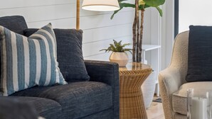 A modern living room with a sofa, armchair, floor lamp, and a large potted plant.