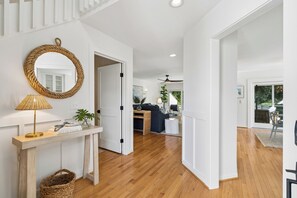 A spacious hallway with wooden flooring, a white wall, and a woven mirror.