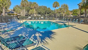 A rectangular pool with a clear blue water, surrounded by lounge chairs and a sandy area.