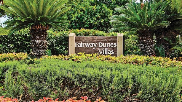 A sign for Fairway Dunes Villas surrounded by lush greenery and ornamental plants.