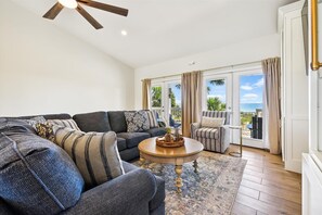 A living room with a dark blue sofa, a round wooden coffee table, and a view of the ocean through large sliding doors.