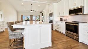 A spacious kitchen with white cabinetry, stainless steel appliances, and a large island. - Welcome to Gulf Dreams! (St. George Island)