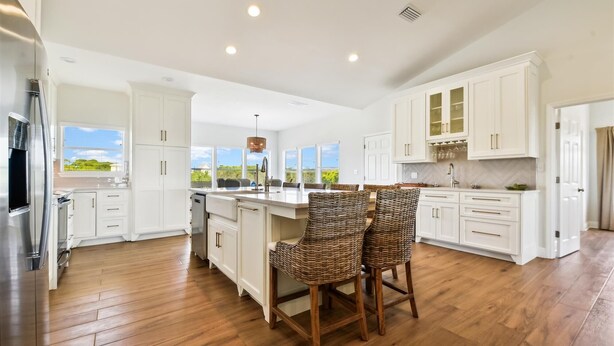 A modern kitchen with white cabinetry, a central island with bar stools, and a view of the outdoors. - Welcome to Gulf Dreams! (St. George Island)