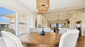 A modern dining area with a round wooden table, six upholstered chairs, and a woven pendant light. - Welcome to Gulf Dreams! (St. George Island)