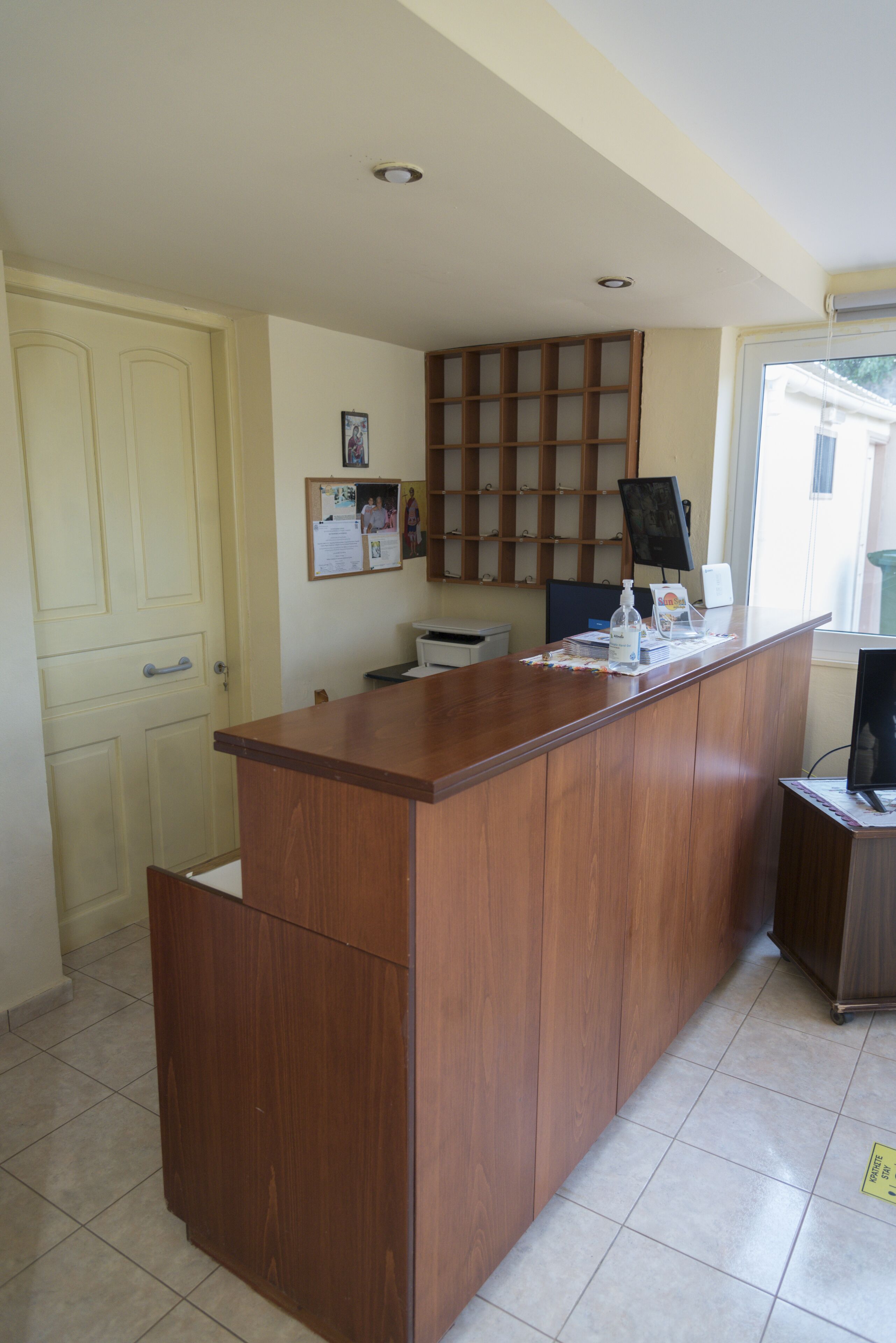 A reception desk with a wooden counter, a bulletin board, and a window with a view of the outside.