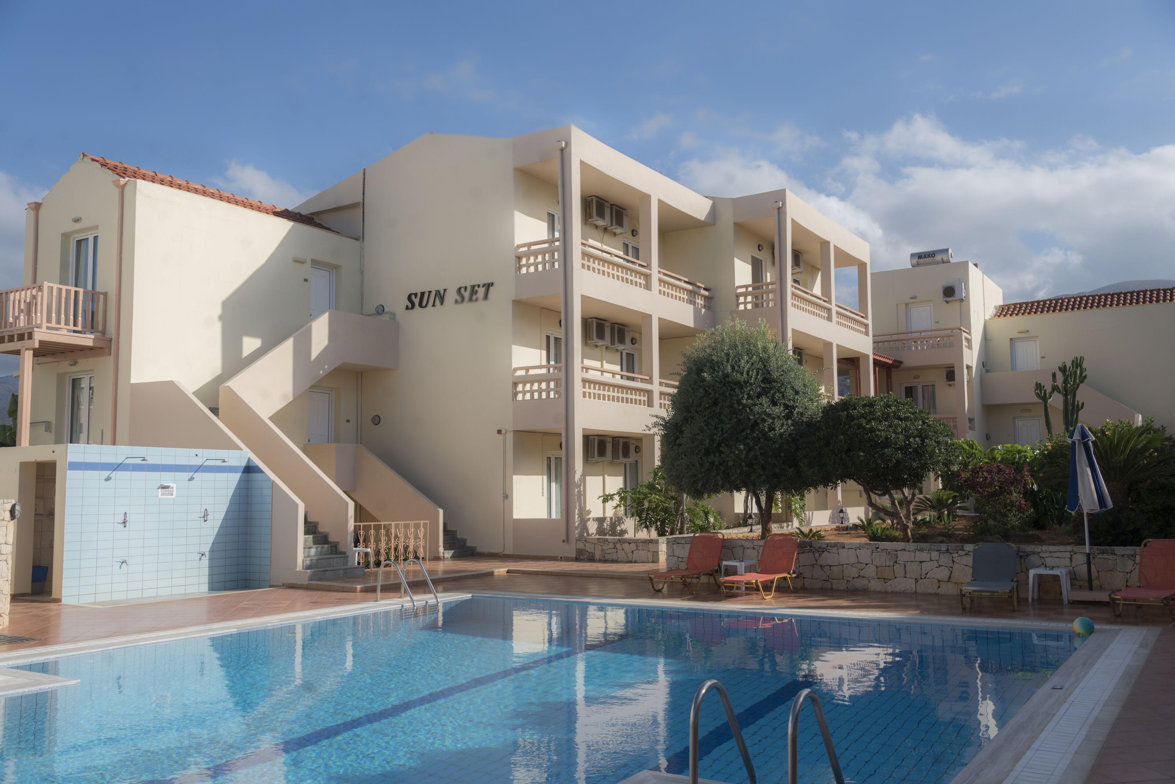 A hotel with a swimming pool, multiple balconies, and a staircase leading to the entrance.