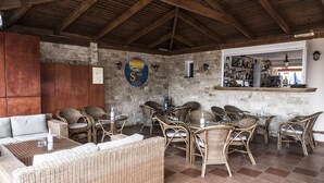 Een rustieke buitenruimte met rieten meubilair, een stenen muur en een bar met flessen op de planken.