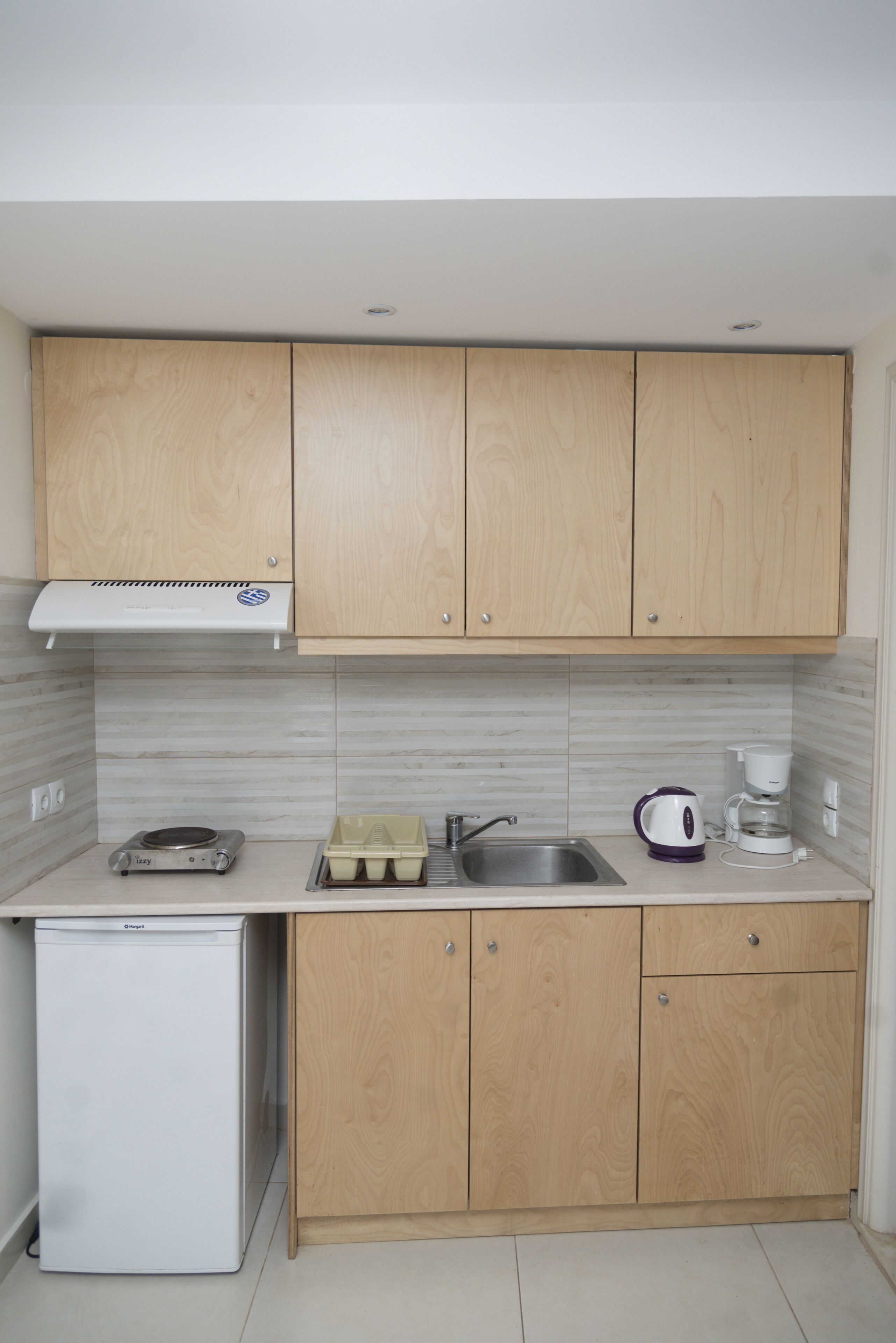 A compact kitchen with wooden cabinets, a built-in oven, a sink, and a coffee maker.