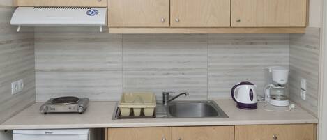 A compact kitchen with wooden cabinets, a built-in oven, a sink, and a coffee maker.