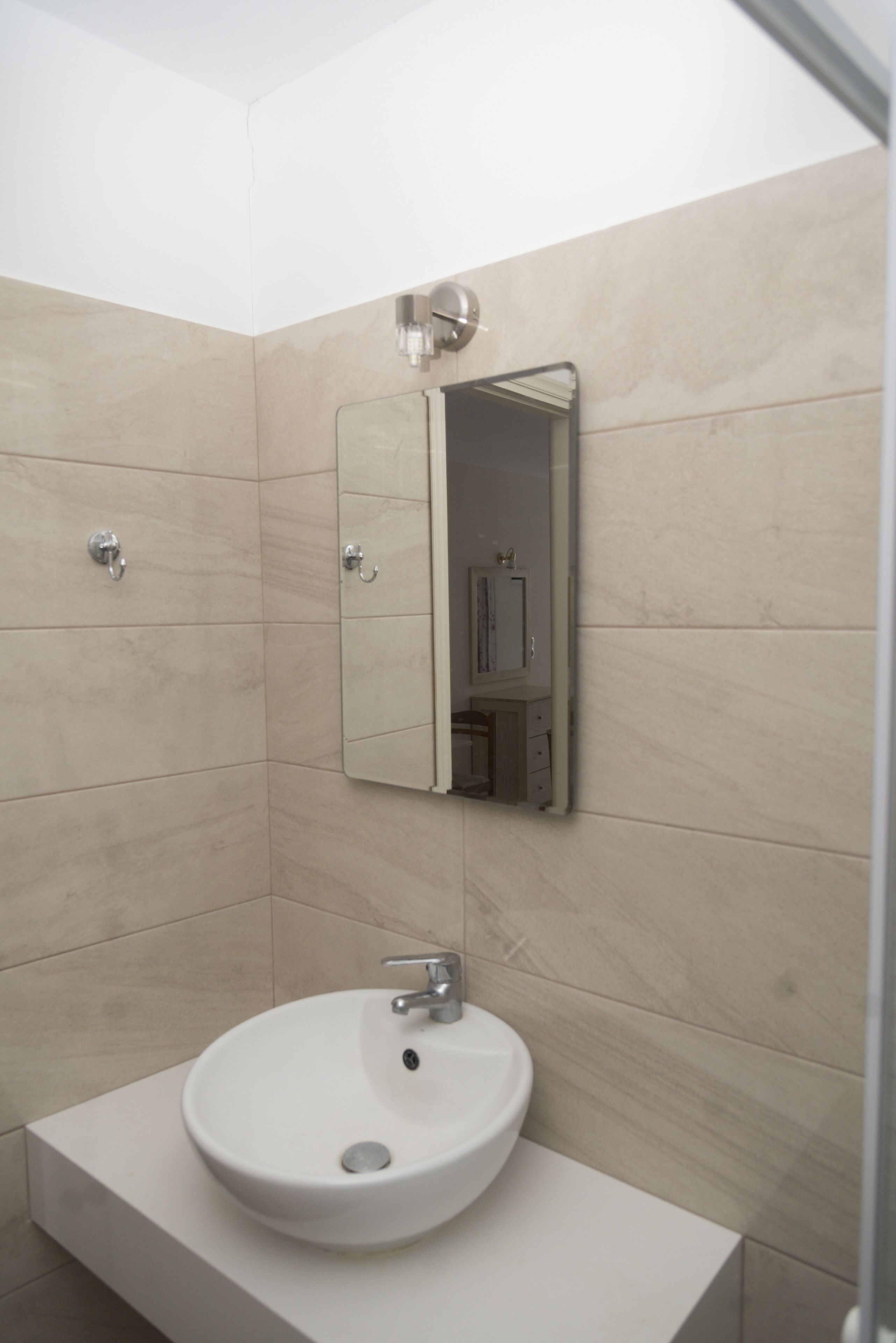 A bathroom with a white sink, a mirror, and beige tiled walls.