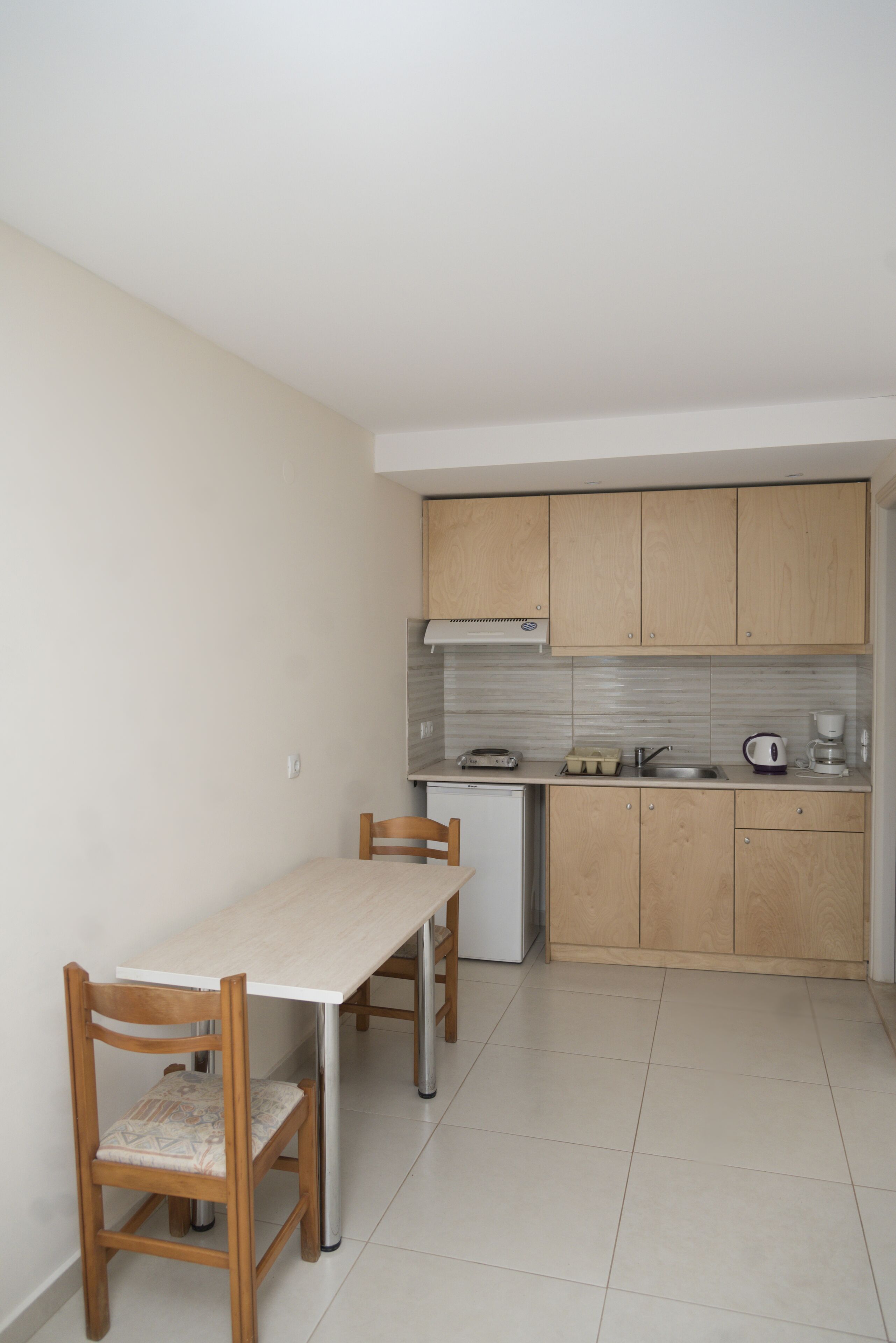 A compact kitchen with a dining table and chairs, a small refrigerator, and wooden cabinets.
