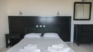 Een net opgemaakt bed met witte lakens en handdoeken, een donker houten hoofdbord, nachtkastjes en een dressoir met laden.