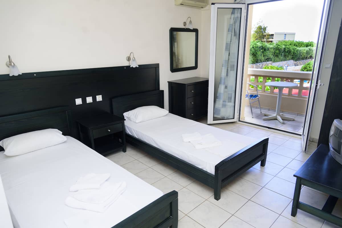 Ein Hotelzimmer mit zwei Betten, einem kleinen Tisch, einem Fernseher und einem Balkon mit Blick auf die Stadt.