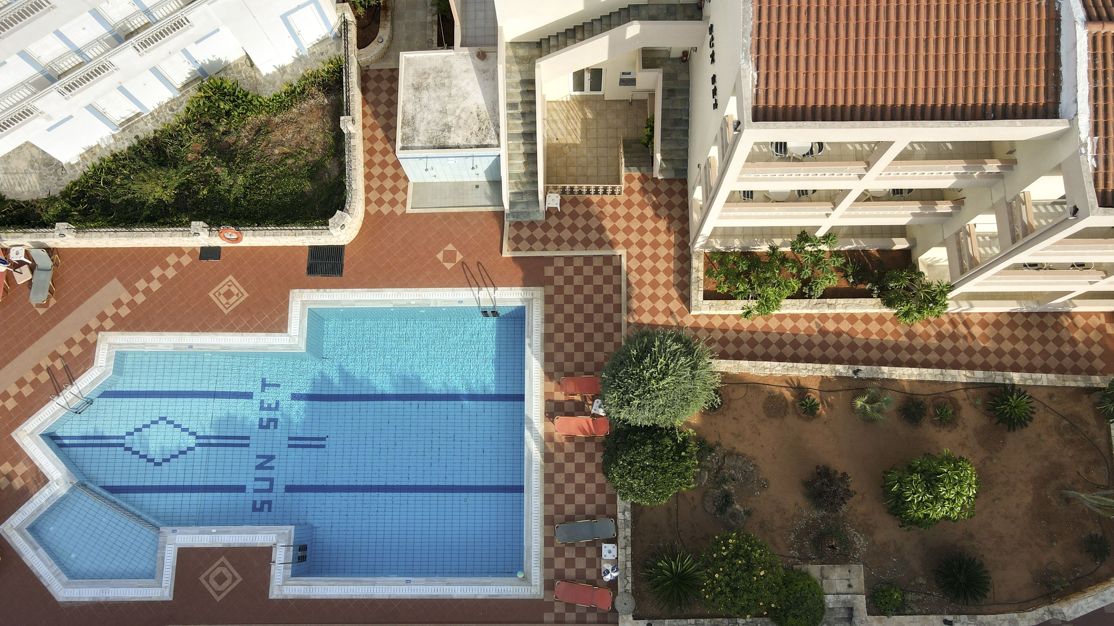 Vista aèria d'un hotel amb piscina, paviment d'escacs i vegetació als voltants.