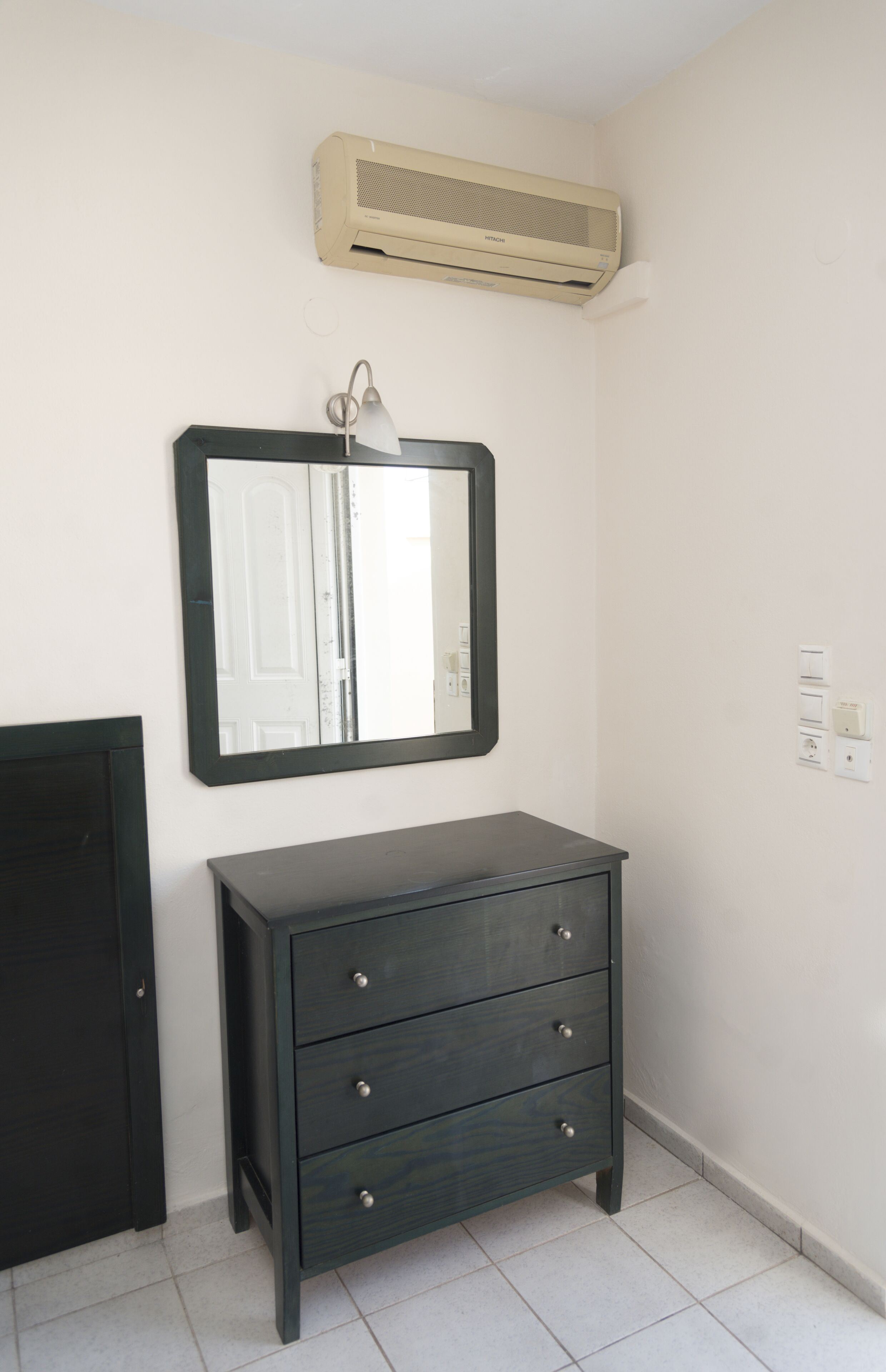 A room with a dark wooden dresser, a mirror, and an air conditioning unit on the wall.