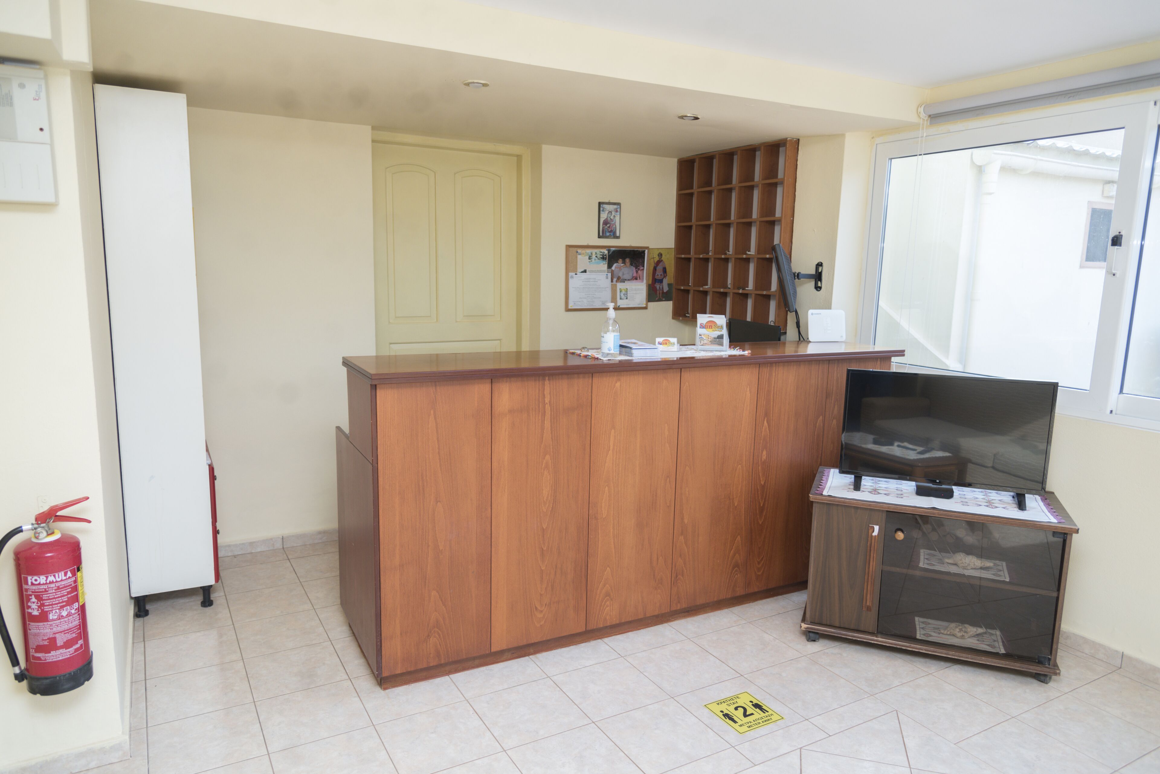A reception desk with a wooden finish, a fire extinguisher mounted on the wall, and a glass display cabinet with a television.