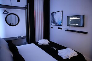 A modern hotel room with a bed, a round mirror, a television, and a wall-mounted artwork. - Dark Boutique Hotel (Dajt)