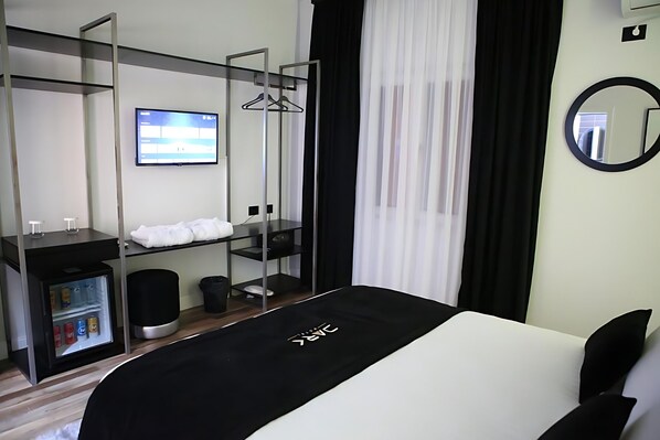 A modern hotel room with a bed, a TV, a mini-fridge, a wardrobe, and a mirror. - Dark Boutique Hotel (Dajt)
