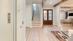 A spacious living area with a staircase, a wooden door, and a kitchen in the background.