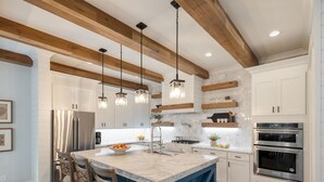 A modern kitchen with a marble island, stainless steel appliances, and wooden beams.