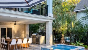An outdoor patio with a dining table and chairs, a pool, and a grill.
