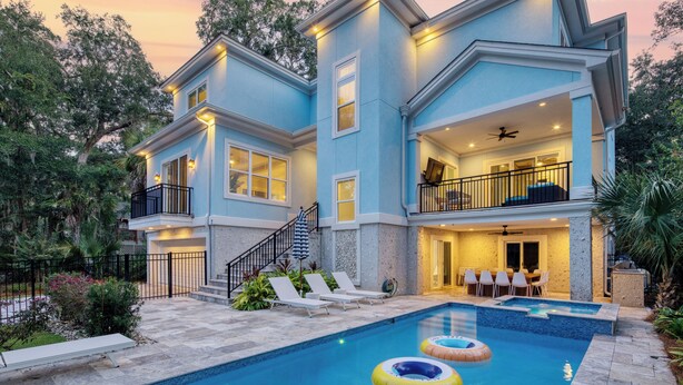 A two-story house with a swimming pool, outdoor seating, and a balcony.