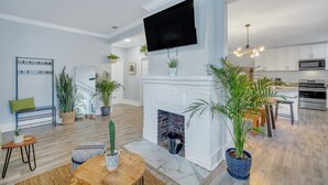 Una sala de estar moderna con chimenea, un televisor de pantalla plana montado encima y una cocina visible a través de un umbral abierto.