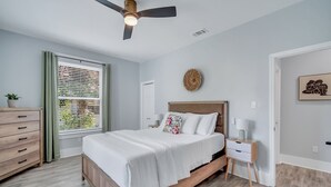 Un dormitorio con cama, mesita de noche, cómoda, ventilador de techo y ventana con persianas.