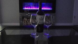 A dark room with a flat-screen TV mounted on the wall, a fireplace with a blue flame, and two wine glasses on a reflective surface. - Perfect getaway to magical Damascus (Damascus)