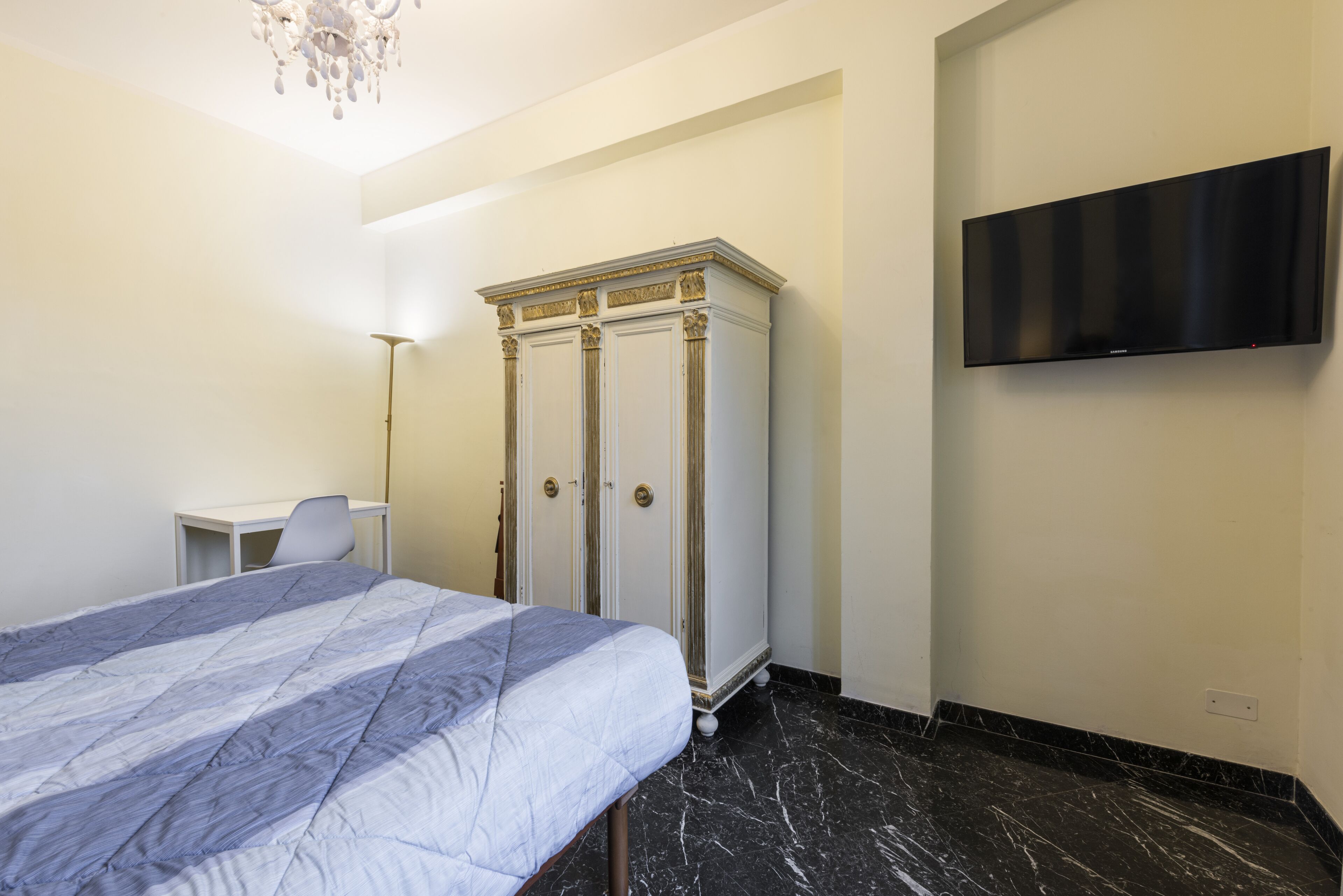 A bedroom with a bed, a wardrobe, a desk, and a flat-screen TV.