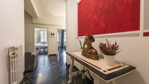 En hall med ett element, en grå soffa, ett bord med en bystskulptur och en krukväxt, samt en röd, abstrakt målning på väggen.