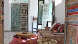 Une pièce avec un sol à motifs, un canapé avec des coussins, une table en bois, un panier en osier et un luminaire suspendu.