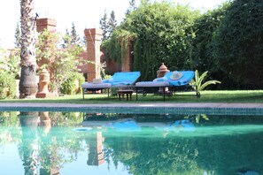 Une piscine avec deux chaises longues, une structure en briques et une végétation luxuriante.
