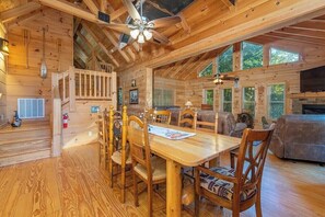 A wooden cabin interior with a dining area, a sofa, and a fireplace.