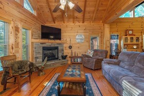 A log cabin interior with a fireplace, wooden walls, a television, and a cozy seating area.