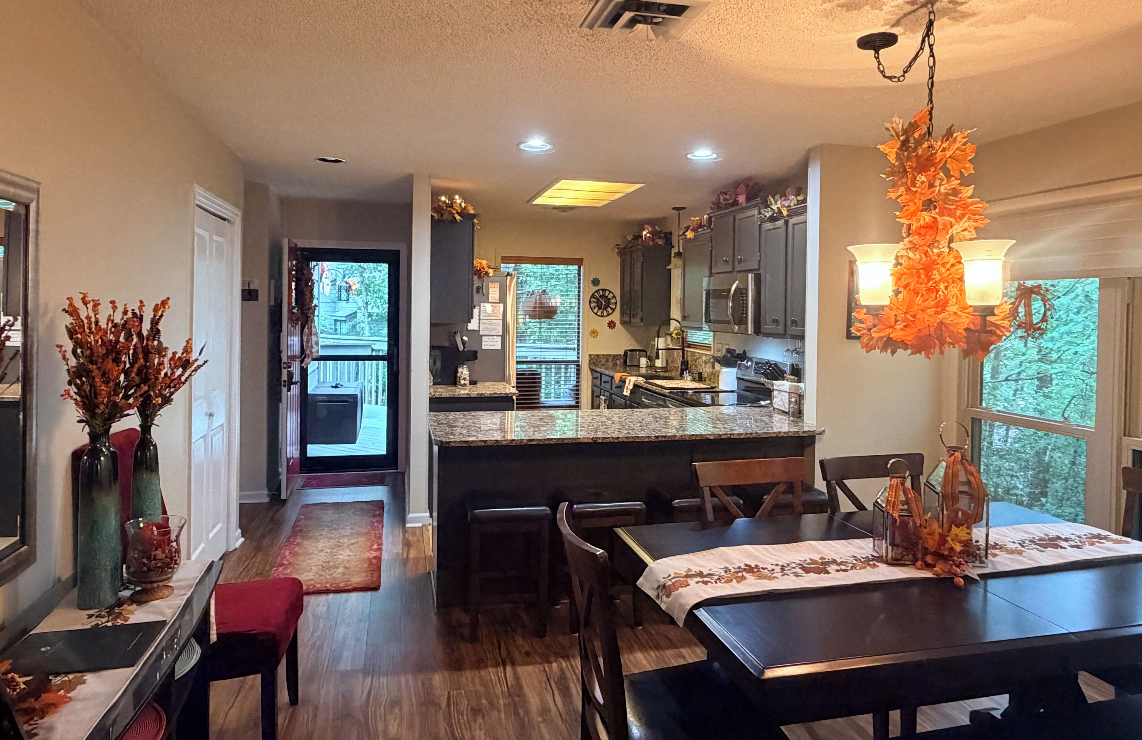 A dining area with a table set for two, a kitchen with modern appliances, and a view of the outdoors through the windows.
