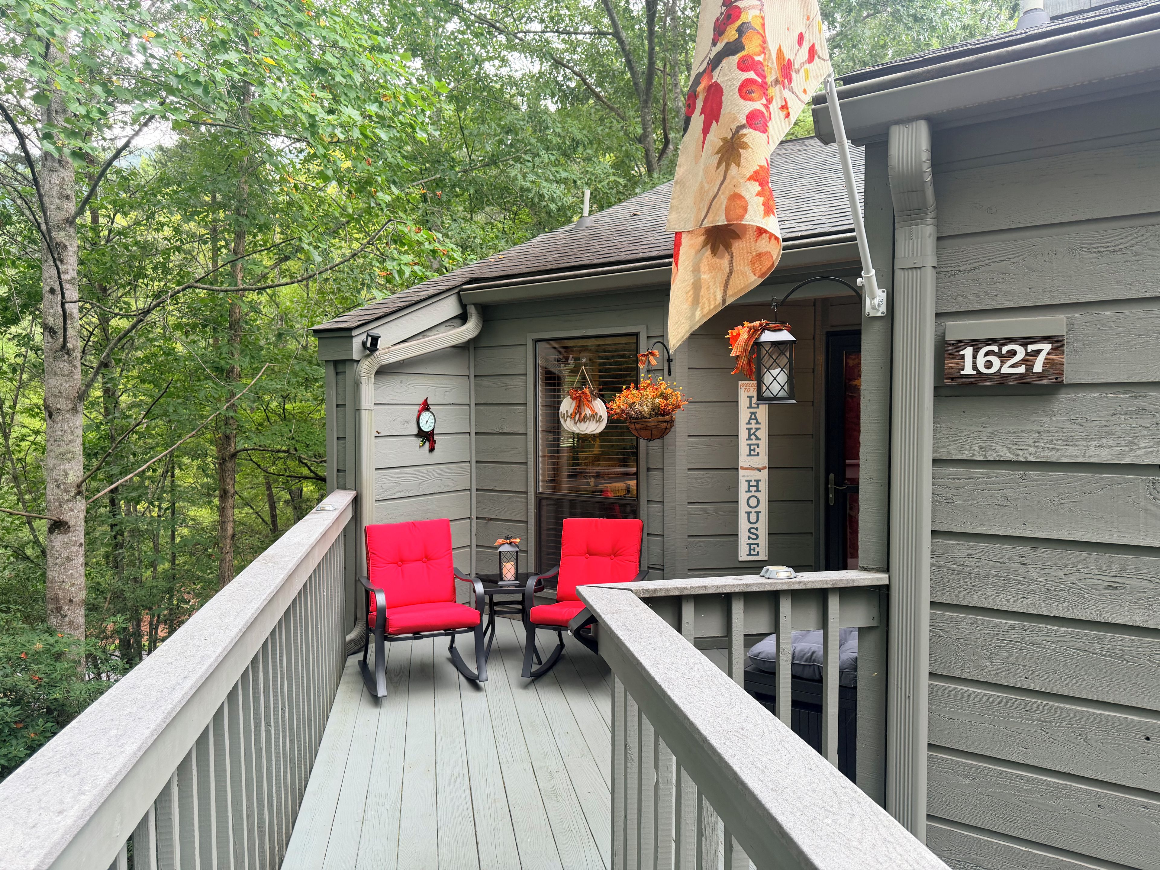 A wooden deck with red chairs and a table, a house number sign, and a hanging lantern with flowers.