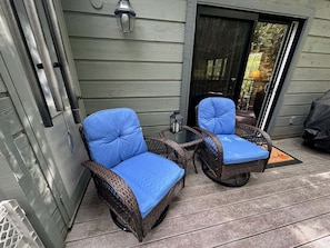 Two wicker chairs with blue cushions on a wooden deck, a lantern, and a sliding glass door.