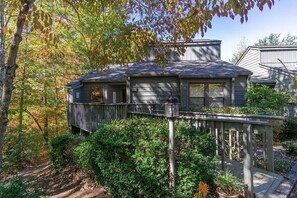 Une maison dotée d’une terrasse, entourée d’arbres et d’arbustes.